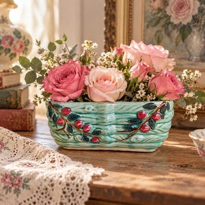 May include: A rectangular ceramic planter with a textured, light green finish resembling wood grain. The exterior is decorated with raised, painted branches featuring dark green leaves and small red berries. It is filled with pink roses.