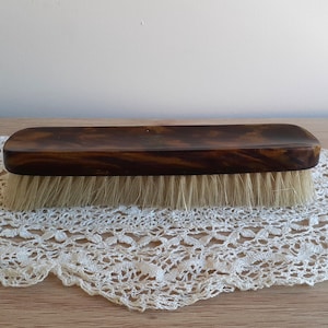 Op de afbeelding: Een bruine houten borstel met witte haren. De borstel ligt op een wit gehaakt doily.