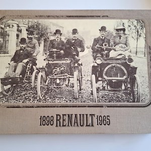 Pode incluir: Uma capa de livro vintage com uma foto em preto e branco de cinco homens com roupas do início do século XX em pé ao lado de quatro carros antigos. O texto da capa diz "1898 RENAULT 1965".