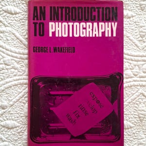 Könnte beinhalten: Eine weiße Keramik-Tasse mit schwarzem Henkel und dem Text "But First, Coffee" in schwarzer, handschriftlicher Schrift. Die Tasse steht auf einer weißen Oberfläche.