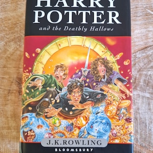 May include: A copy of "Harry Potter and the Deathly Hallows" by J.K. Rowling. The book cover displays Harry, Ron, and Hermione, with a golden sun and magical items. The publisher is Bloomsbury.