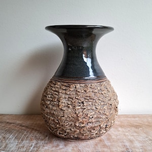 May include: A ceramic vase with a textured, bark-like exterior in shades of brown and tan. The top portion is a glossy, dark teal colour. The vase has a wide base and a flared, dark teal rim.