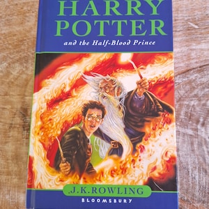 May include: A hardback book titled "Harry Potter and the Half-Blood Prince" with a blue cover and green text. The cover art depicts Harry Potter, a wizard, and fiery imagery. The author, J.K. Rowling, and publisher, Bloomsbury, are also shown.