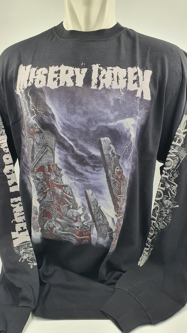May include: Black long-sleeve t-shirt with a graphic print of a skeletal figure in front of a stormy sky. The text "Misery Index" is printed across the top of the shirt. The text "Veritas" is printed on the graphic. The text "The Walls Of Power" is printed on the left sleeve.