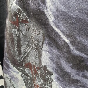May include: Black and white graphic t-shirt with a skull and lightning bolts. The text "Veritas" is visible on the shirt.
