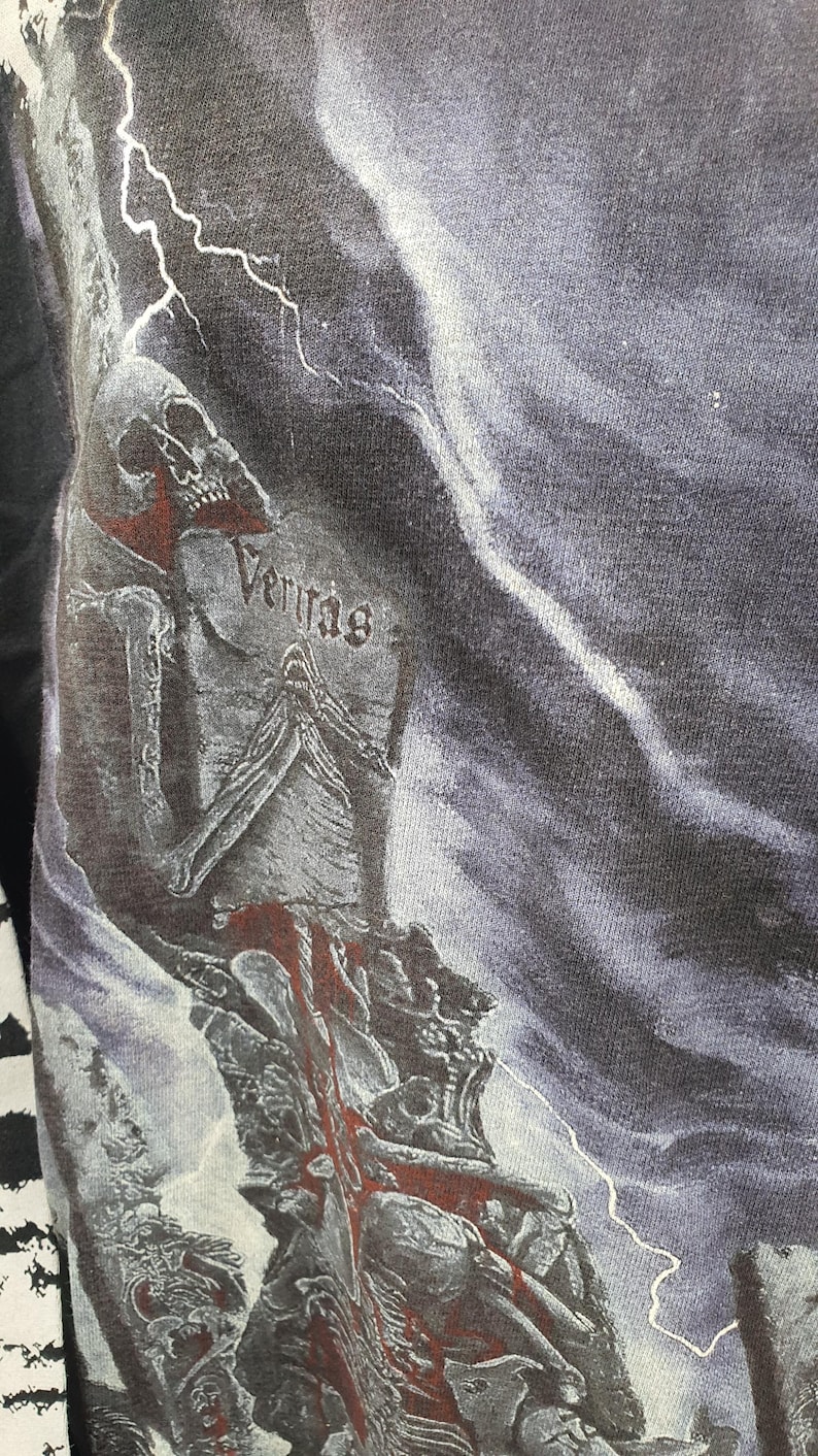May include: Black and white graphic t-shirt with a skull and lightning bolts. The text "Veritas" is visible on the shirt.