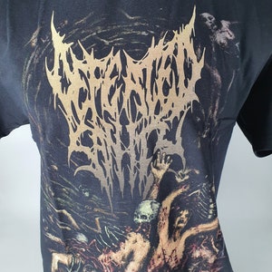 Puede incluir: Camiseta negra con un estampado gráfico de un logotipo de banda, "INCANTATION", en letras doradas. El gráfico también presenta una imagen espeluznante de una persona con múltiples brazos y cráneos.