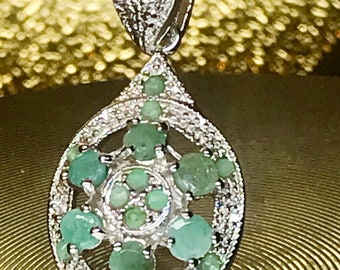 May include: A silver pendant necklace with a teardrop-shaped design featuring a cluster of green gemstones surrounded by smaller white gemstones.