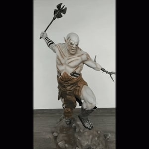 K&ouml;nnte beinhalten: Eine wei&szlig;e Orc-Figur mit einem braunen Lendenschurz und einer Axt aus Metall, die auf einem felsigen Sockel steht.
