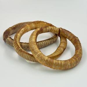 May include: Three circular, dried dog treats in shades of brown and tan are arranged on a white surface. The treats have a textured, ridged appearance, and are likely made from natural ingredients.