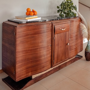Könnte beinhalten: Ein antiker Holzschrank mit einer schwarzen Marmorplatte. Der Schrank hat zwei Türen und eine Schublade mit einem goldenen Griff. Auf der Oberseite befinden sich zwei Bücher und eine Schale mit Orangen.