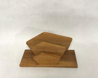 May include: A wooden napkin holder with a geometric design. The holder is made of three stacked pieces of wood, each with a different shape.