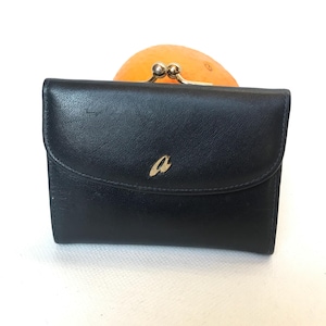 May include: Black leather wallet with a flap closure and a gold-colored 'a' emblem. The wallet has a kiss-lock clasp and a curved top. The wallet is a small, compact size, suitable for carrying essential items.