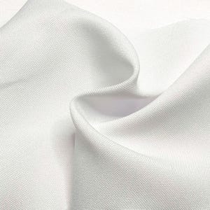 May include: Close-up of white fabric with a textured weave. The fabric is folded, creating soft curves and shadows. The material appears to be a medium-weight textile, suitable for clothing or home decor.