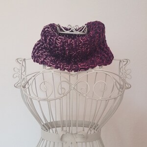 Op de afbeelding: Een paars en roze gebreide cowl neck sjaal getoond op een wit metalen mannequin.