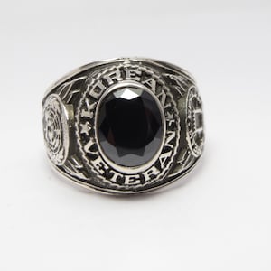 May include: Silver-toned ring with a large, oval black stone at the center. The ring is engraved with the words "KOREAN VETERAN" and features decorative details on the sides. A classic piece of jewelry.