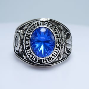 May include: A silver ring with a blue gemstone and the inscription "UNITED STATES COAST GUARD".