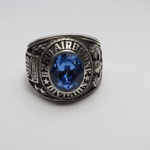 Peut inclure: Une bague en argent avec une pierre bleue et l'inscription "82nd Airborne Division".