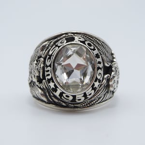 Peut inclure: Une bague de classe en argent avec une grosse pierre transparente et l'inscription "High School 1955".