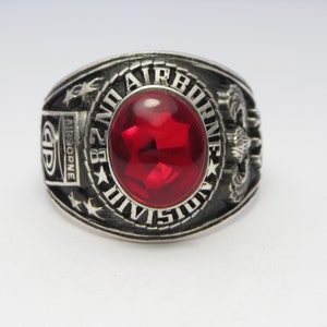 Peut inclure: Une bague en argent avec une pierre rouge et l'inscription "82nd Airborne Division".