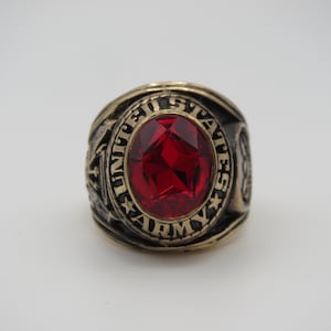 Peut inclure: Une bague en or avec une pierre précieuse rouge et l'inscription "UNITED STATES ARMY" autour de la bande.