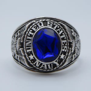 May include: A silver ring with a blue gemstone and the words "United States Navy" engraved on it.
