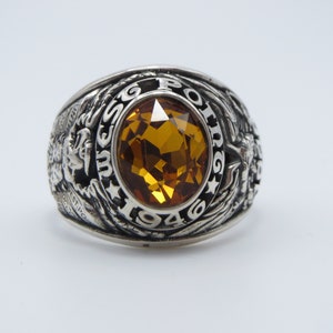 Peut inclure: Une bague de classe en argent avec une pierre précieuse orange et l'inscription "USSG 1949" sur la bande.