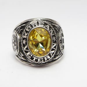 May include: A silver ring with a yellow gemstone and the inscription "KOREAN VETERAN" around the stone.