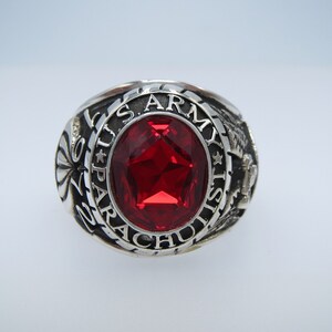 Peut inclure: Une bague en argent avec une pierre précieuse rouge et l'inscription "U.S. ARMY PARACHUTIST".