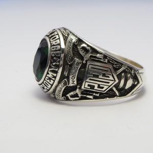 May include: Silver class ring with a green gemstone and the inscription "ACADEMY FORGE & MY HONOR COURAGE CONQUER". The ring also features a shield with the letters "E.G." and crossed swords.