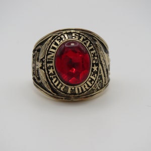Peut inclure: Une bague en or avec une pierre rouge et l'inscription "United States Air Force".