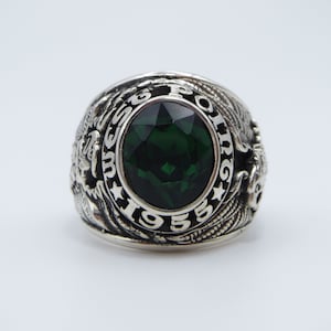 Peut inclure: Une bague en argent avec une grosse pierre précieuse verte et l'inscription "USMC 1955" autour de la pierre.