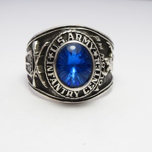 May include: A silver ring with a blue gemstone and the inscription "U.S. ARMY INFANTRY FOLLOW ME CENTURIES"
