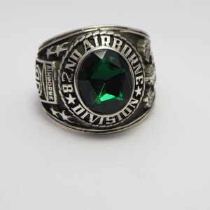 Peut inclure: Une bague en argent avec une pierre précieuse verte et l'inscription "82nd Airborne Division".