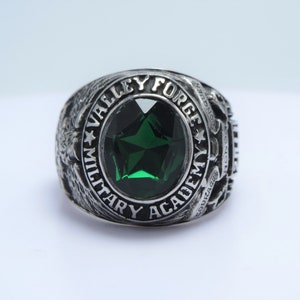Op de afbeelding: Een zilveren ring met een groene edelsteen en de inscriptie "Valley Forge Military Academy" rond de band.