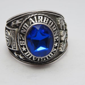Peut inclure: Une bague en argent avec une pierre précieuse bleue et l'inscription "28th Airborne" sur la bande.