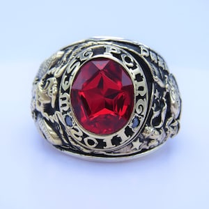 Op de afbeelding: Een gouden en zilveren ring met een grote rode edelsteen en de inscriptie "USMC 1920 11".
