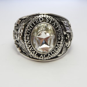 May include: A silver ring with a large clear stone and the inscription "UNITED STATES NAVAL ACADEMY".