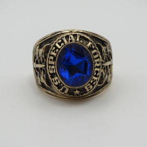 Peut inclure: Une bague en or avec une pierre précieuse bleue et l'inscription "U.S. SPECIAL FORCES".