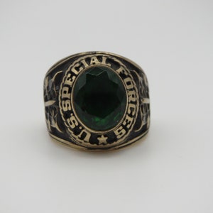 Peut inclure: Une bague en or avec une pierre précieuse verte et l'inscription "U.S. SPECIAL FORCES" autour de la bande.