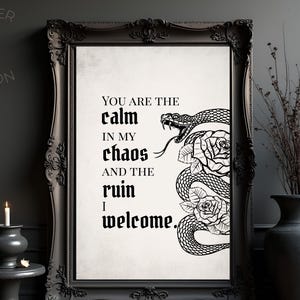 以下が含まれることがあります： 「YOU ARE THE calm IN MY chaos AND THE ruin I welcome」のテキストが入った黒いフレームのアートプリント。 蛇とバラの白黒イラストがプリントの右側にあります。