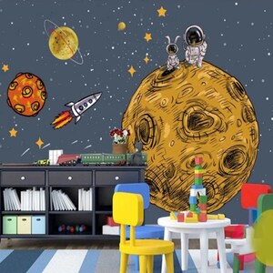 K&ouml;nnte beinhalten: Ein gelber und brauner Cartoon-Planet mit zwei Astronauten, die oben drauf stehen. Der Planet ist von Sternen und einer Rakete umgeben. Der Hintergrund ist dunkelblau mit wei&szlig;en Sternen.