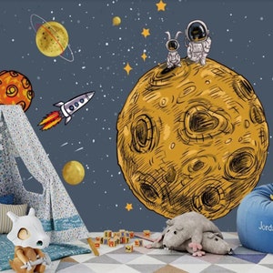 K&ouml;nnte beinhalten: Ein blaues und gelbes Wandbild zum Thema Weltraum mit einer Rakete, Planeten, Sternen und zwei Astronauten, die auf einem gro&szlig;en Mond stehen. Das Wandbild befindet sich in einem Raum mit einem Tipi, einem Stofftier und einem Sitzsack.