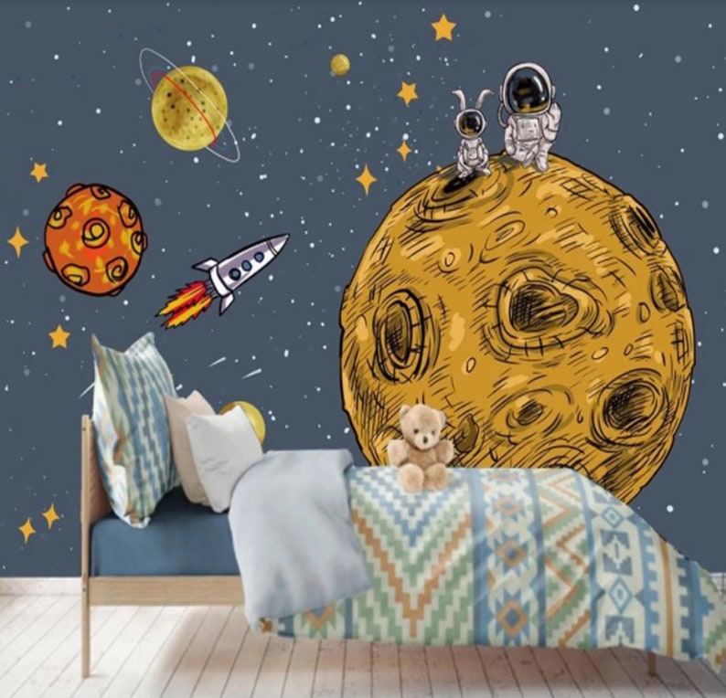 K&ouml;nnte beinhalten: Ein blaues und gelbes Wandbild f&uuml;r ein Kinderzimmer mit Weltraumthema mit einem gro&szlig;en gelben Mond, zwei Astronauten, einer Rakete und Sternen.