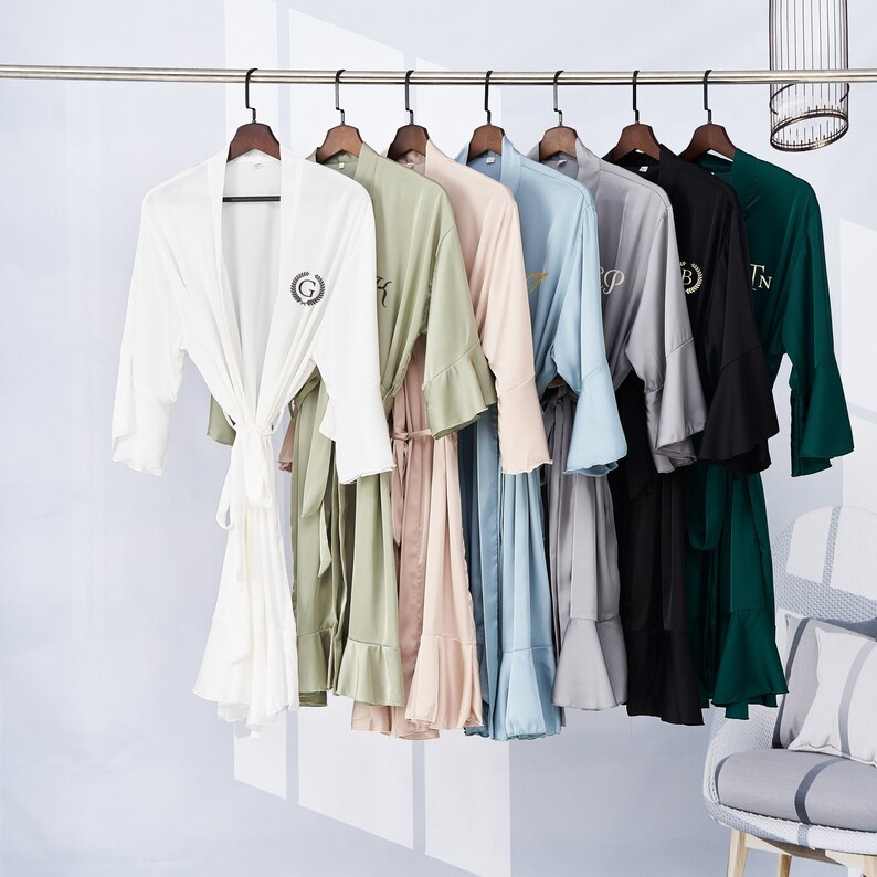 May include: A set of eight robes in various colors, each with a different embroidered initial. The robes have ruffled edges and are hung on hangers.