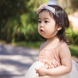 May include: A young girl wearing a white tulle dress with a pink bodice and a flower headband. The dress has a pink flower embellishment on the bodice. The girl is looking to the right of the frame. The text "Tiny Minnie Boutique" is visible at the bottom of the image.