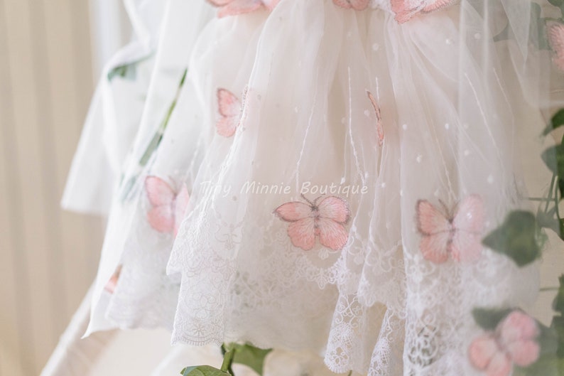 May include: White tulle dress with pink butterfly embroidery and a white lace trim. The dress has a dotted pattern and the text "Tiny Minnie Boutique" is visible.