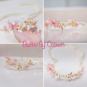 May include: A delicate gold headband with pink butterfly accents, white flowers, and pearl-like beads. The headband is on a white background.