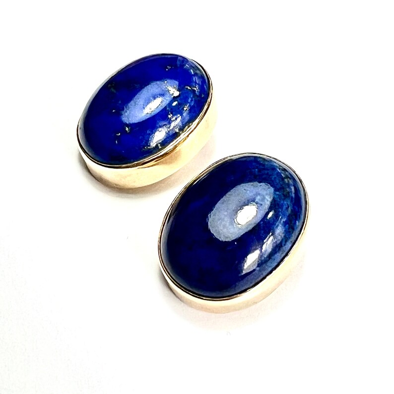 K&ouml;nnte beinhalten: Ein Paar ovale Lapislazuli-Ohrringe, die in Gold gefasst sind. Die Ohrringe sind tiefblau mit goldenen Flecken.