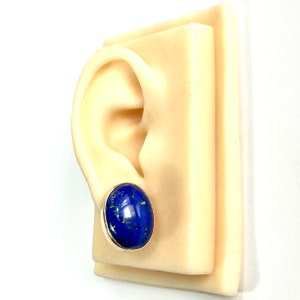 K&ouml;nnte beinhalten: Ein Paar goldene Ohrstecker mit ovalen Lapislazuli-Steinen. Die Ohrringe sind an einem Ohrmodell zu sehen.
